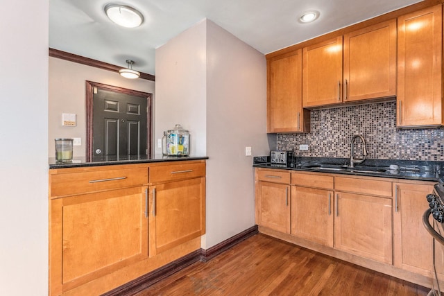 kitchen featuring crown molding, dark hardwood / wood-style flooring, sink, backsplash, and dark stone counters