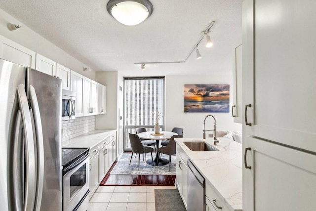 kitchen featuring white cabinetry, stainless steel appliances, tasteful backsplash, light stone countertops, and sink