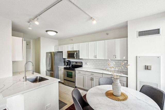 kitchen with kitchen peninsula, backsplash, stainless steel appliances, white cabinetry, and sink