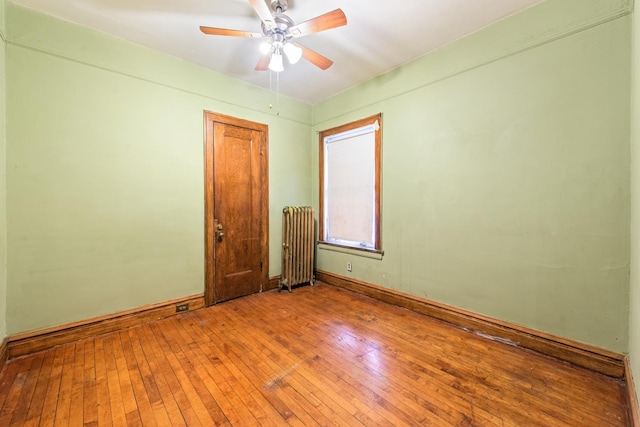 empty room with hardwood / wood-style flooring, ceiling fan, and radiator heating unit