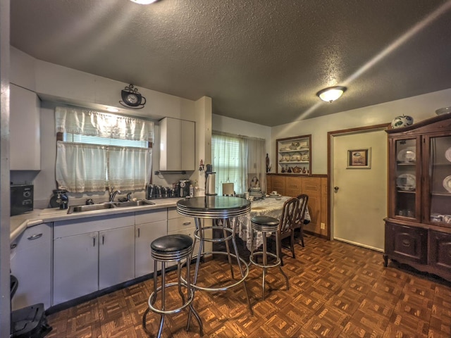 kitchen featuring a textured ceiling, white cabinetry, dark parquet flooring, and sink