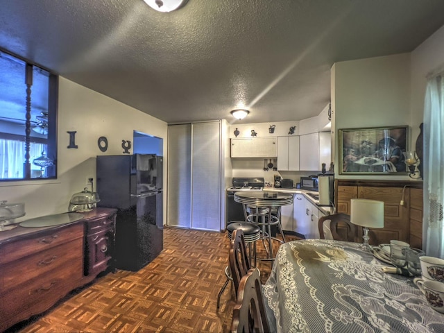 interior space featuring a textured ceiling, dark parquet flooring, white cabinets, and black appliances