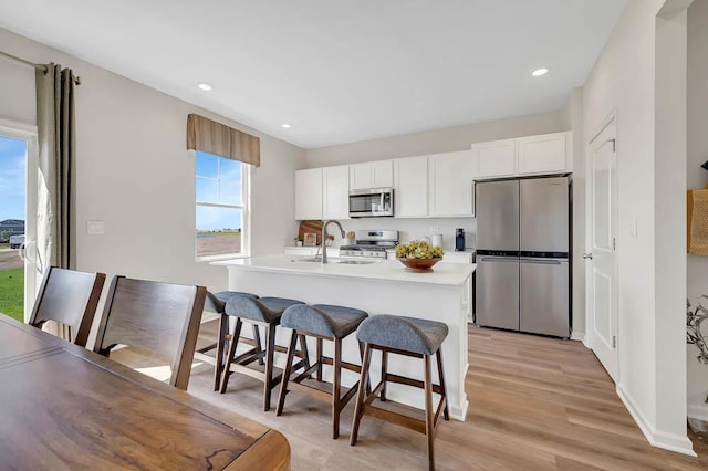 kitchen with white cabinetry, a kitchen bar, a center island with sink, stainless steel appliances, and light hardwood / wood-style flooring