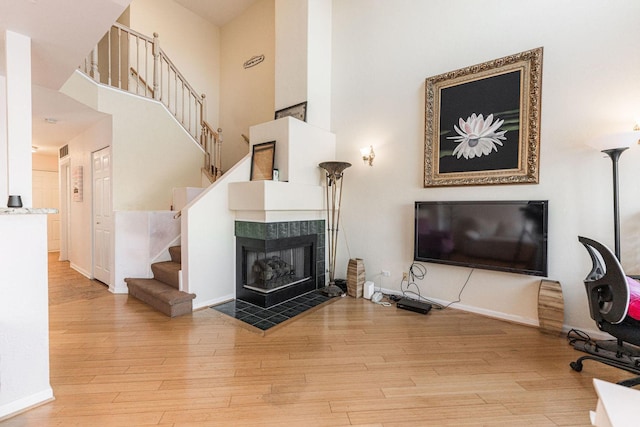 living room featuring light hardwood / wood-style floors, a high ceiling, and a tile fireplace