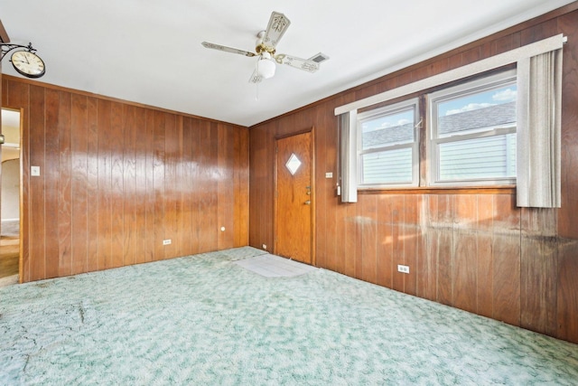 carpeted foyer with ceiling fan and wooden walls