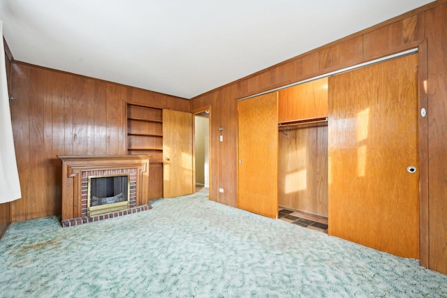 unfurnished living room with a fireplace, built in shelves, carpet floors, and wood walls