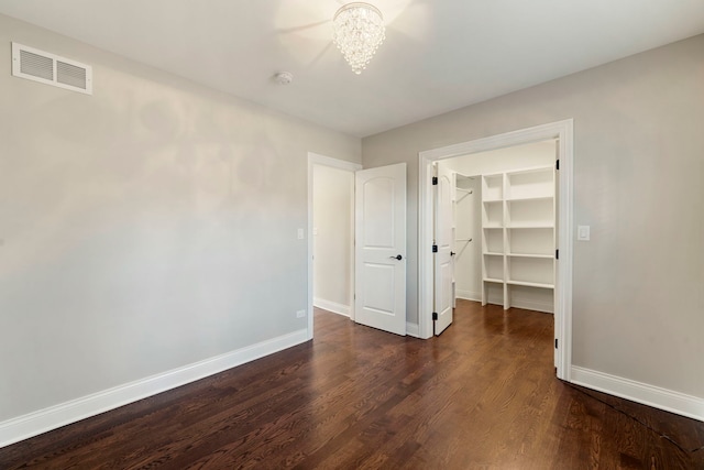 unfurnished bedroom with a spacious closet, a closet, a chandelier, and dark hardwood / wood-style floors