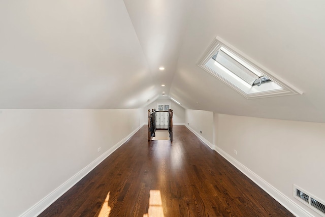 additional living space with vaulted ceiling with skylight and dark wood-type flooring