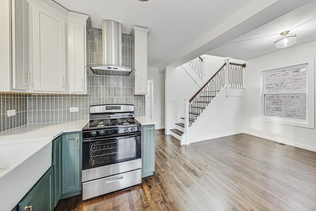 kitchen with tasteful backsplash, stainless steel gas range oven, green cabinets, white cabinets, and wall chimney exhaust hood