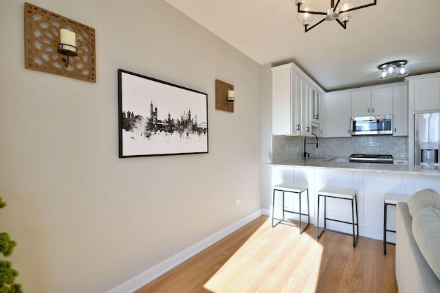 kitchen featuring white cabinetry, tasteful backsplash, a chandelier, light wood-type flooring, and appliances with stainless steel finishes