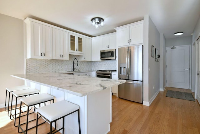 kitchen featuring white cabinetry, light stone counters, a breakfast bar area, and stainless steel appliances