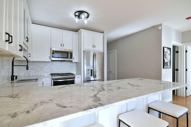 kitchen featuring sink, a breakfast bar area, stainless steel appliances, decorative backsplash, and white cabinets