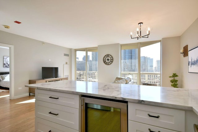 kitchen with wine cooler, light wood-type flooring, light stone counters, and white cabinets