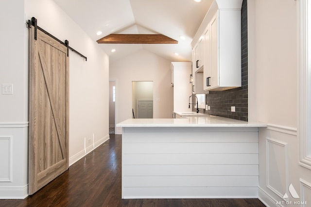 kitchen with white cabinetry, sink, kitchen peninsula, lofted ceiling with beams, and a barn door