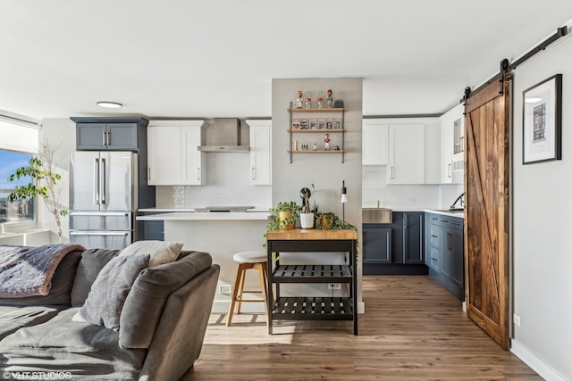 kitchen featuring a barn door, high end fridge, a breakfast bar area, tasteful backsplash, and wall chimney exhaust hood