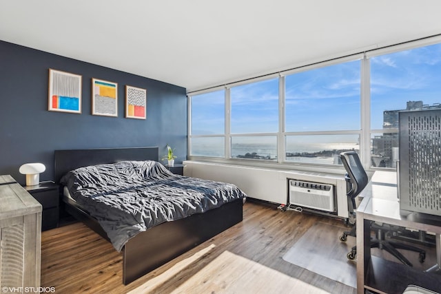 bedroom with a water view, hardwood / wood-style flooring, and a wall mounted air conditioner