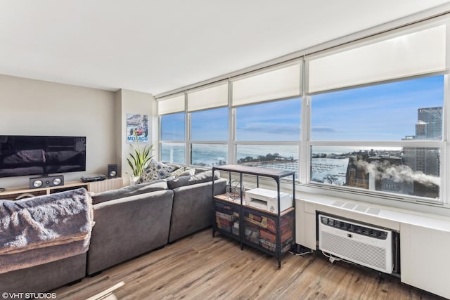 living room with floor to ceiling windows, light hardwood / wood-style floors, a water view, and a wall mounted air conditioner