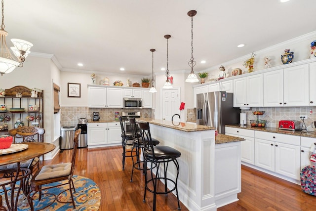 kitchen with white cabinets, a breakfast bar area, appliances with stainless steel finishes, hardwood / wood-style floors, and hanging light fixtures