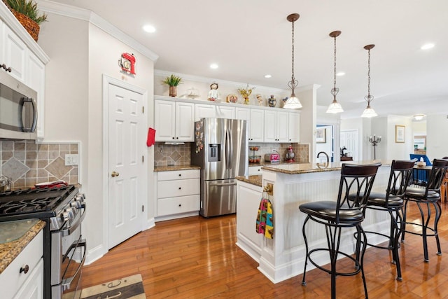 kitchen with light wood finished floors, an island with sink, appliances with stainless steel finishes, a breakfast bar area, and white cabinetry