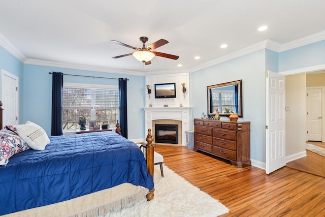 bedroom featuring a large fireplace, recessed lighting, baseboards, wood finished floors, and ornamental molding