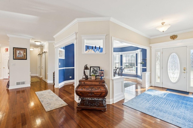 foyer entrance featuring ornamental molding, wood-type flooring, visible vents, and a barn door