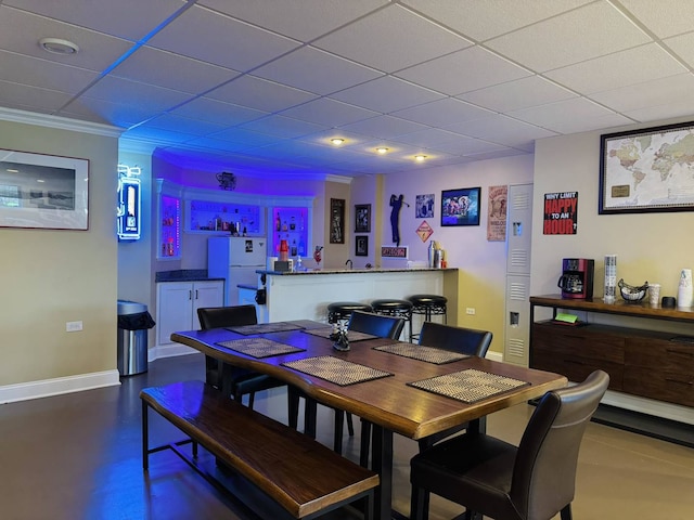 dining space featuring concrete floors, a paneled ceiling, baseboards, ornamental molding, and a bar