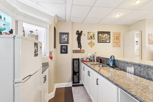 kitchen featuring freestanding refrigerator, baseboards, white cabinetry, light stone counters, and a sink