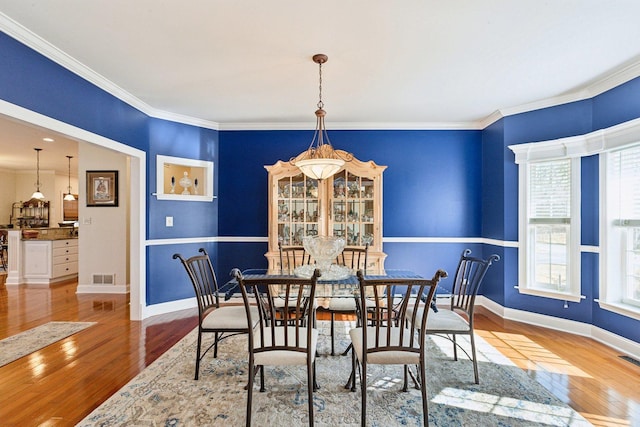 dining room featuring visible vents, crown molding, baseboards, and hardwood / wood-style flooring