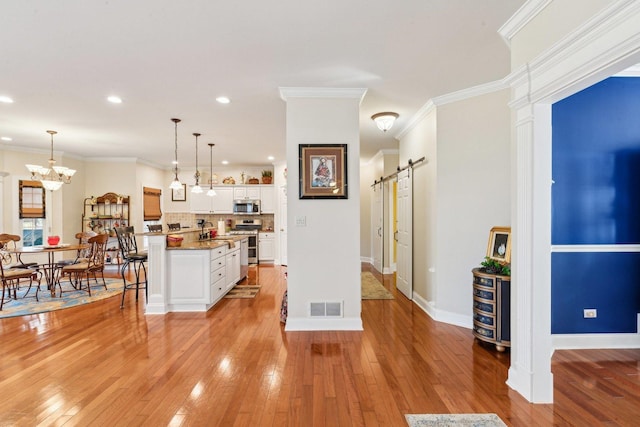 kitchen featuring a breakfast bar area, visible vents, a barn door, stainless steel appliances, and white cabinetry