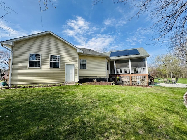 back of house with a sunroom, roof mounted solar panels, a lawn, and a patio