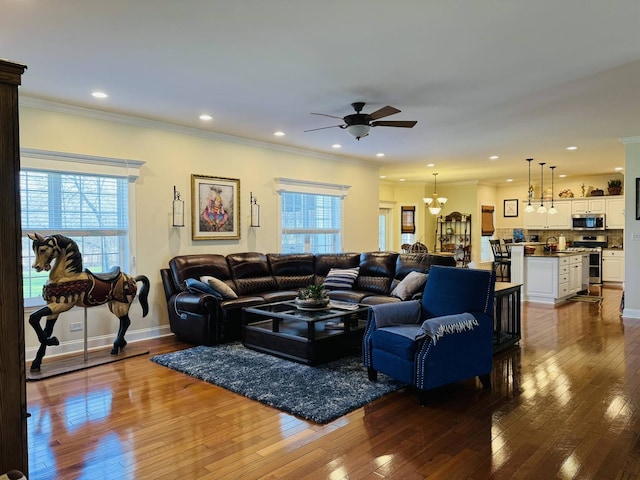 living room featuring crown molding, plenty of natural light, ceiling fan with notable chandelier, and dark wood-type flooring