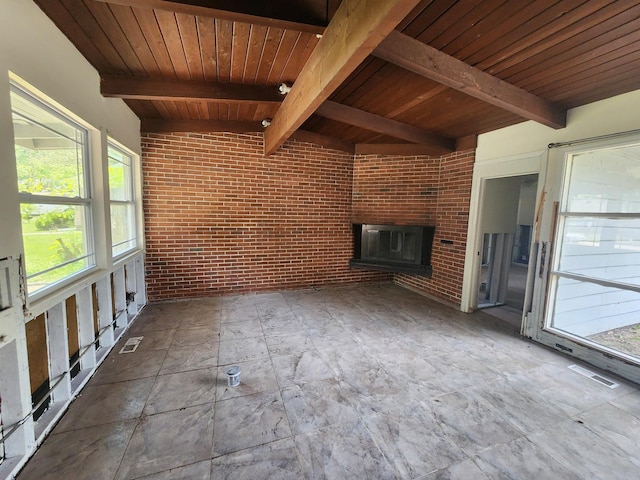 unfurnished living room featuring a brick fireplace, wooden ceiling, brick wall, and vaulted ceiling with beams