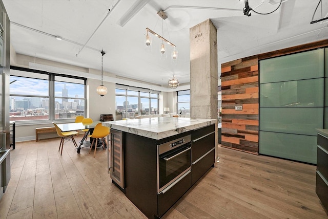 kitchen with oven, light hardwood / wood-style floors, wooden walls, hanging light fixtures, and beverage cooler