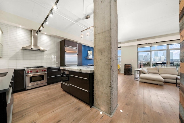 kitchen with decorative light fixtures, wall chimney range hood, light hardwood / wood-style floors, decorative backsplash, and high end appliances