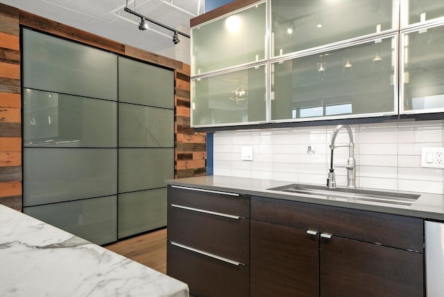 kitchen featuring tasteful backsplash, sink, dark brown cabinetry, dishwashing machine, and light stone counters