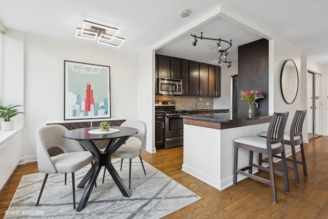 kitchen featuring a breakfast bar area, backsplash, dark wood-type flooring, stainless steel appliances, and dark brown cabinets