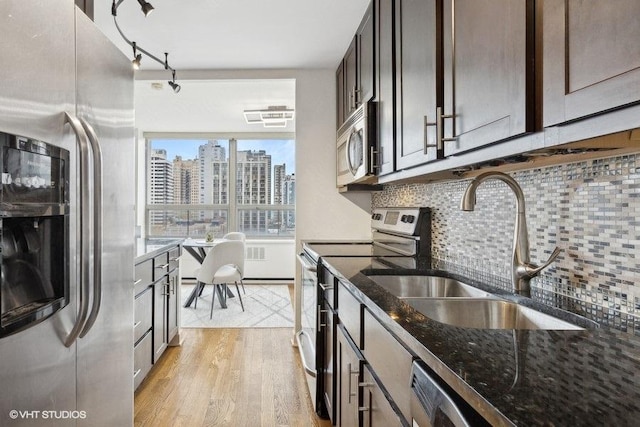 kitchen featuring sink, appliances with stainless steel finishes, light hardwood / wood-style floors, decorative backsplash, and dark stone counters