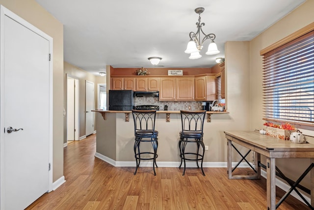 kitchen featuring a kitchen bar, kitchen peninsula, a notable chandelier, light wood-type flooring, and light brown cabinetry