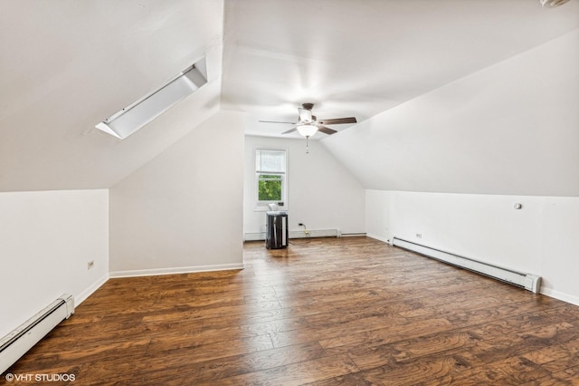 additional living space featuring ceiling fan, vaulted ceiling with skylight, dark hardwood / wood-style flooring, and a baseboard radiator