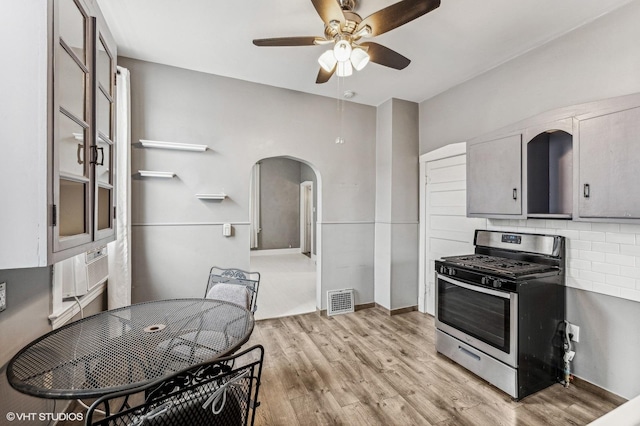 kitchen with gray cabinets, ceiling fan, backsplash, light wood-type flooring, and gas range