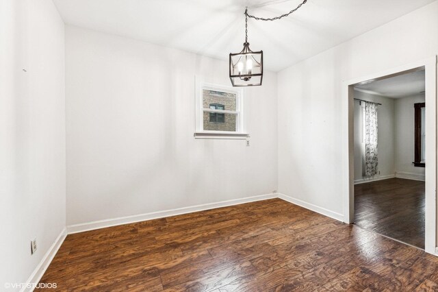 spare room featuring dark hardwood / wood-style flooring and a notable chandelier