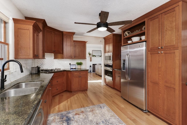 kitchen with a textured ceiling, appliances with stainless steel finishes, dark stone counters, light hardwood / wood-style floors, and sink