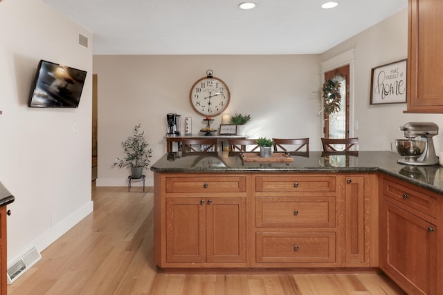 kitchen with kitchen peninsula, dark stone counters, and light wood-type flooring