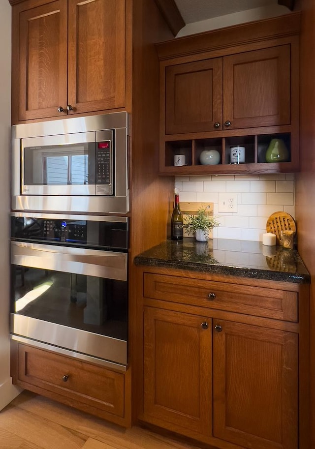 kitchen with light wood-type flooring, decorative backsplash, dark stone counters, and stainless steel appliances