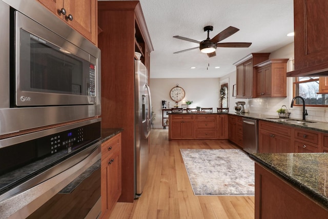 kitchen with appliances with stainless steel finishes, tasteful backsplash, dark stone countertops, sink, and light hardwood / wood-style flooring