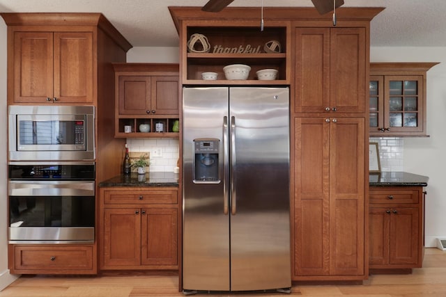 kitchen with appliances with stainless steel finishes, light wood-type flooring, dark stone counters, a textured ceiling, and decorative backsplash