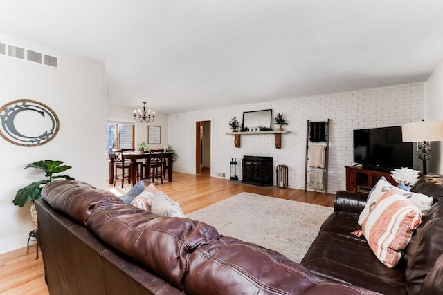 living room with light wood-type flooring, a chandelier, brick wall, and a brick fireplace