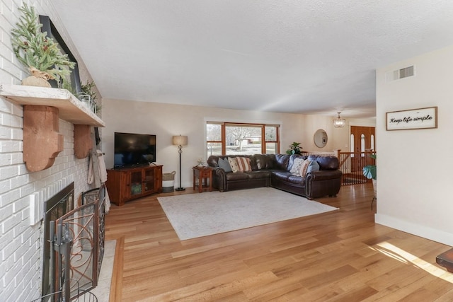 living room featuring light hardwood / wood-style floors, a textured ceiling, and a brick fireplace