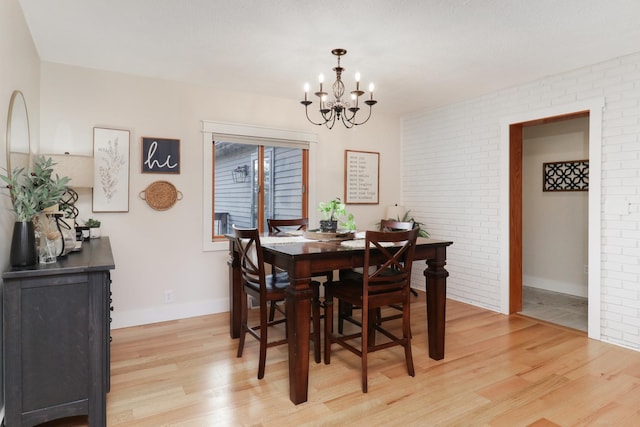 dining room featuring light wood-type flooring, brick wall, and a notable chandelier