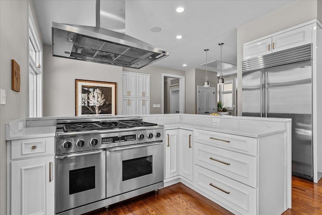 kitchen with high end appliances, wood-type flooring, kitchen peninsula, island exhaust hood, and white cabinets